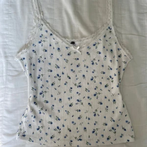 Blommig spetskantad linnetopp🤍 - Supersöt vit linnetopp med blått blommönster och spetskant runt halsringningen! Dekorerad med en liten rosett framtill🫶🏼. Hör av dig om du har någon fundering!💭
