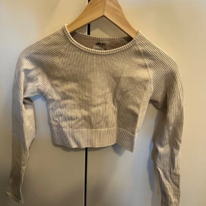 Beige ribbad croppad långärmad topp från Aim'n - Säljer en beige ribbad croppad långärmad topp från Aim'n. Toppen har rund halsringning och är tillverkad i ett stretchigt material med diskreta ränder. Perfekt för en trendig och avslappnad stil.