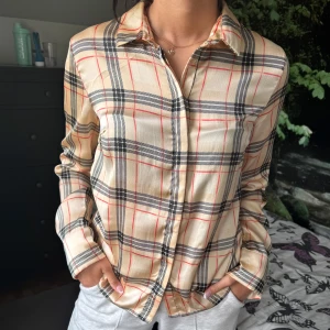 Beige rutig skjorta - Snygg beige skjorta med klassiskt rutigt mönster i svart, rött och vitt. Skjortan har långa ärmar, krage och knäppning framtill. Köpt från Vero Moda i storlek S