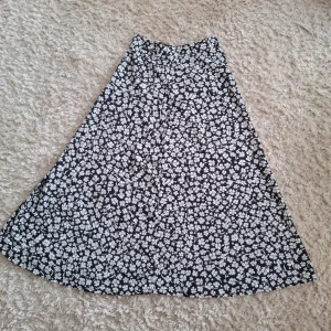 Svart blommig kjol från Amisu - Långkjol från Amisu med vitt blommigt mönster. Kjolen har en lätt utställd passform!