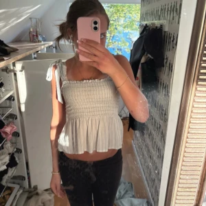 Vit blus med knytaxlar från Nelly - Supersöt vit blus från Nelly med smockad överdel och volang nertill. Axelbanden knyts i rosetter och tyget har tunna ränder. 