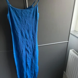 Blå ribbad långklänning med slits - Säljer en blå ribbad långklänning med smala axelband och slits nertill. Klänningen har en tight passform och är perfekt för sommardagar. Enkel och stilren design som är lätt att matcha med accessoarer.