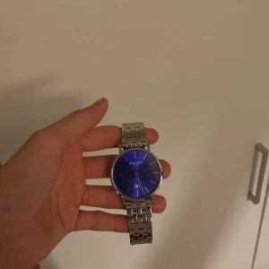 Lorenzo Milano herrklocka med blå urtavla - Stilren herrklocka från Lorenzo Milano med blå urtavla och silverfärgat armband i metall. Klockan har minimalistisk design med romerska siffror. Levereras med originalfodral och extra länkar. Alla delar som är med på bilderna kommer med. Lite repig vid Lorenzo Milano märket annars väldigt bra skick. Ordinarie pris: 1699, Mitt pris: 450. Bara att höra av er vid frågor😊
