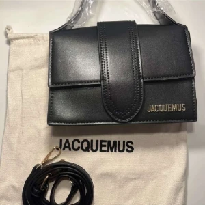 Svart axelväska från Jacquemus - Säljer en stilren svart axelväska från Jacquemus med guldigt logotyptryck. Väskan har en avtagbar axelrem och stängs med ett brett lock. Tillverkad i slätt skinn och levereras med dustbag.💕Pris kan diskuteras 