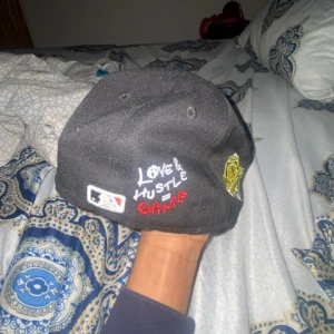 Svart Atlanta Braves keps World Series - Svart keps med Atlanta Braves-logga framtill, World Series 1995-märke på sidan och broderad texten 'Love & Hustle Game' baktill. Klassisk basebollkeps med böjd skärm och broderade detaljer.