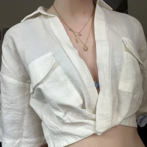 Vit croppad linneskjorta med fickor - Säljer en vit croppad skjorta i linne med två stora bröstfickor och korta ärmar. Skjortan har en avslappnad passform och är perfekt för varma dagar. Enkel och stilren design som passar till jeans eller kjol.