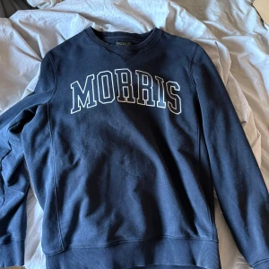 Mörkblå sweatshirt från Morris - Klassisk mörkblå sweatshirt från Morris med vit text på bröstet. Tröjan har rund halsringning, långa ärmar och ribbade muddar vid ärmslut och nederkant. Perfekt för en avslappnad och stilren look. Säljes då jag rensat ur min garderob storlek M men passar även om du har S :)