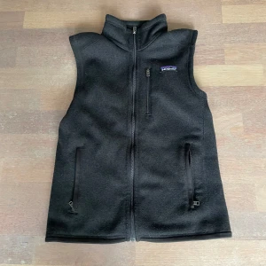 Patagonia väst - Säljer en svart fleeceväst från Patagonia med hög krage och hel dragkedja framtill. Västen har två sidofickor med dragkedja och en bröstficka med dragkedja. Perfekt för lager-på-lager och outdoor.