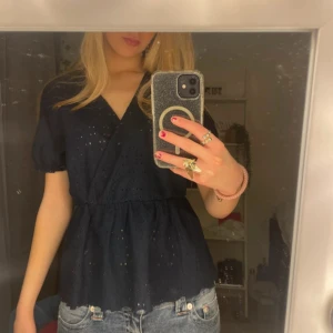 Mörkblå blus med v-ringning - Säljer en mörkblå blus med v-ringning och korta puffärmar. Blusen har broderade detaljer och en lätt volang nertill. Perfekt att styla med jeans för en snygg look💕💕