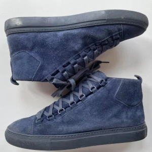 ARENA SKOR - Säljer ett par mörkblå sneakers i mocka med högt skaft och platt svart sula. Skorna har rund tå och klassisk snörning hela vägen upp. Perfekta för dig som gillar stilrena och bekväma skor med en modern touch.