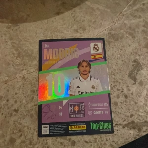 Fotbollssamlarbilder Luka Modric Real Madrid - Två samlarkort med Luka Modric från Real Madrid. Ena kortet har holografiska detaljer och visar statistik, det andra har svartvit bild med grön text 'Winner'. Perfekt för samlare av fotbollskort och Real Madrid-fans.