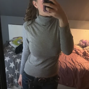 Grå polotröja i ribbstickad bomull - Säljer en enkel och stilren grå polotröja med lång ärm. Tröjan är ribbstickad i midjan, vid ärmslut och i halsen vilket ger en snygg passform. Perfekt till jeans eller kjol. Vet inte riktigt om storlek 