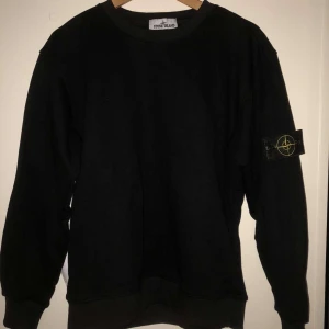Svart tröja från Stone Island - Säljer en svart tröja från Stone Island med klassisk rund hals och märket på vänster ärm. Tröjan har ribbade muddar vid ärmslut och nederkant. Perfekt för en stilren och avslappnad look. Tveka inte för att skriva vid minsta funderingar!