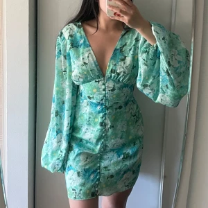 Blommig klänning från Adoore - Kollar intresset på denna superfina, slutsålda klänningen i grönt blommigt mönster från Adoore. Kortare modell. Klänningen har långa puffärmar, knappar framtill och markerad midja. Så drömmig nu till sommaren!🌸🌿☀️Endast använd en gång. Funderar på att sälja för att köpa den längre modellen istället🩷Storlek 36!