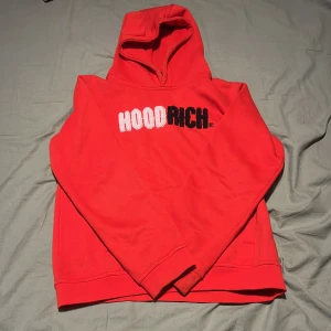 Röd hoodie från Hoodrich - Säljer en röd hoodie från Hoodrich med broderad logga i vitt och svart på bröstet. Tröjan har huva och en klassisk passform. Perfekt för dig som gillar streetwear och vill sticka ut med en färgstark look.