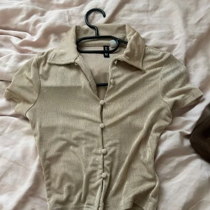 Beige kortärmad skjorta med knappar - Säljer en beige skjorta med korta ärmar och stora knappar framtill. Skjortan har en klassisk krage och är tillverkad i ett mjukt, lätt material.