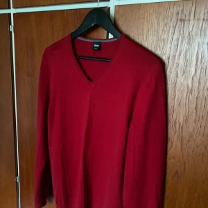 Röd v-ringad tröja från Hugo Boss - Röd långärmad tröja från Hugo Boss med v-ringad hals. Enkel och stilren design, perfekt med skjorta under. Mjuk och bekväm, passar till många olika tillfällen. 