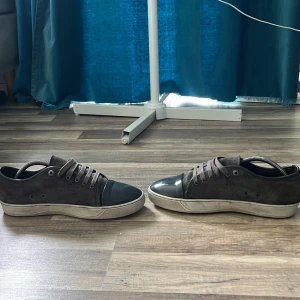  Lanvin med grå toe box och grå sko - Säljer ett par grå sneakers från Lanvin med grå tåparti i glansigt material och grå mocka på sidorna. Skorna har snörning och platt vit sula. Perfekta för dig som gillar stilrena och exklusiva sneakers. 41 men passar också 42 är hål i sulan 