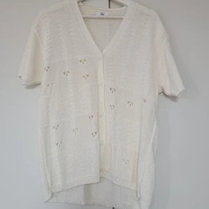 Vit stickad kofta med kort ärm från Gianetti Maria Bon - Säljer en söt vit stickad kofta med korta ärmar och v-ringning. Koftan har knappar framtill och små hålmönster som ger en luftig känsla. Perfekt att slänga över en topp när det är lite kyligt ute.