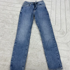 Blå raka jeans med hög midja - Klassiska blå jeans med rak passform och hög midja. Jeansen har fem fickor, dragkedja och knapp framtill samt tydliga sömmar. Perfekta för en avslappnad och tidlös stil.