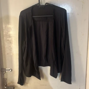 Svart öppen cardigan  - Säljer en svart, tunn och öppen cardigan med lång ärm. Koftan har en enkel och stilren design utan knappar eller dragkedja, perfekt att slänga över en topp eller t-shirt.
