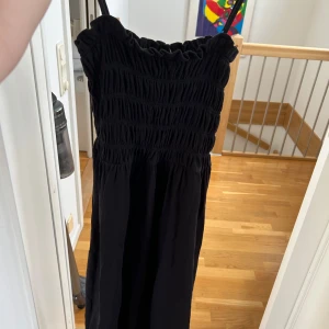 Svart långklänning med smock - Säljer en svart långklänning med smockad överdel och tunna axelband. Klänningen har en luftig passform och är perfekt för varma dagar. Enkel och stilren design som passar till många tillfällen. Från hm storlek xs