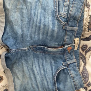 Blå jeansshorts från Lindex - Säljer dem på grund av att jag inte använder dem längre. Det är ett par klassiska blå jeansshorts från Lindex med normal passform. Shortsen har fem fickor, bälteshällor och justerbar midja med knappresår. Perfekta för sommardagar och enkla att matcha med olika toppar.