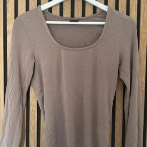 Beige långärmad topp med rund hals - Säljer en enkel och stilren beige långärmad topp med rund halsringning. Toppen är i ett mjukt och stretchigt material som sitter tight mot kroppen. Perfekt att matcha med jeans eller kjol för en clean look.