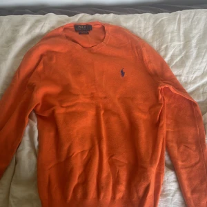 Orange tröja från Polo Ralph Lauren - Säljer en orange tröja från Polo Ralph Lauren med rund halsringning och klassisk broderad logga på bröstet. Tröjan har långa ärmar och ribbade muddar vid ärmslut och nederkant. Perfekt för dig som gillar stilrena plagg med färg.