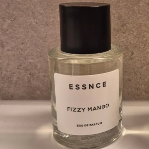 ESSNCE Fizzy Mango Eau de Parfum - En fräsch och fruktig parfym med doft av mango från ESSNCE. Flaskan är genomskinlig med en enkel vit etikett och svart lock. Perfekt för dig som gillar tropiska och livliga dofter. Sprayad en gång.