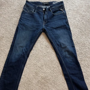Mörkblå jeansbyxor Replay Rocco - Säljer ett par mörkblå jeans från Replay, modell Rocco Comfort Fit. Klassisk femficksdesign med dragkedja och knapp framtill. Snygga slitningar och detaljer på bakfickorna. Perfekta för dig som gillar en tidlös jeanslook.
