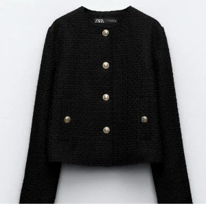 Svart kavajjacka med guldknappar från Zara - Stilren svart kavajjacka från Zara med dekorativa guldknappar framtill. Jackan har rund halsringning, lång ärm och en elegant, strukturerad textur. Perfekt för att lyfta vilken outfit som helst.