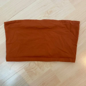 Rostbrun tubtopp - Säljer en enkel och stilren rostbrun tubtopp i mjukt material. Perfekt att matcha med jeans eller kjol för en avslappnad look. Toppen är axelbandslös och har en tight passform.