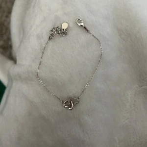 Silverarmband med hjärta från SNÖ - Säljer ett tunt och elegant silverarmband från SNÖ med ett hjärtformat hänge dekorerat med små glittriga stenar. Perfekt detalj för att lyfta din outfit. Justerbar längd med karbinlås.