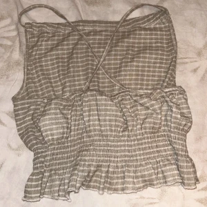 Beige/vit topp med band som korsas i ryggen - Säljer en söt croppad linnetopp från Gina Tricot i beige och vitt randigt mönster. Toppen har smala axelband som korsas i ryggen❤️Säljer eftersom att jag inte gillar croppade toppar 🙌Toppen säljs inte längre