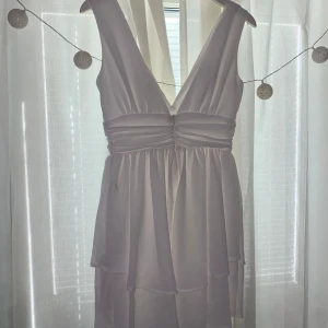 Vit omlottklänning med djup v-ringning - Säljer en vit omlottklänning med djup v-ringning både fram och bak. Klänningen har breda axelband och markerad midja med lätt rynk. Kjolen är luftig och har lager på lager-effekt. Perfekt för sommarens tillfällen!