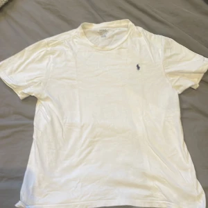Vit t-shirt från Polo Ralph Lauren - Klassisk vit t-shirt från Polo Ralph Lauren med liten broderad logga på bröstet. T-shirten har rund hals och korta ärmar, perfekt för en clean och stilren look. Den är i storlek L för barn så passar XS.
