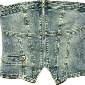 Jeans korsett-topp med dragkedja - Cool jeans korsett-topp i ljusblå denim med dragkedja framtill och dekorativ ficka med dragkedja. Snygga sömdetaljer och markerad midja ger en trendig look. Perfekt för att lyfta din outfit! Har använts en gång och är i väldigt bra skick. Köpt på new yorker.