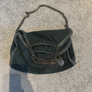 Grön axelväska från Stella McCartney - Säljer min gröna axelväska från Stella McCartney som jag älskar men som inte kommer till så mycket användning längre. Den är köpt begagnad men är i väldigt bra skick, har dock en liten slitning på framsidan, se bild 3, men som inte syns när man har den på sig. Skriv för fler bilder eller mått😊