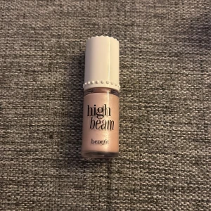 High Beam flytande highlighter från Benefit - High Beam från Benefit är en flytande highlighter i en ljusrosa, skimrande nyans. Kommer i en liten flaska med vit kork och pärldetaljer. Perfekt för att ge glow till kindben, näsrygg och amorbåge.