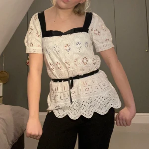 Vit blus  - Superfin vit blus, broderad och med svarta detaljer vid halsringning och midja. Blusen har korta puffärmar, knytband i midjan och vågig nederkant. Perfekt för en söt och trendig look!
