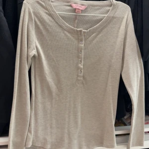Ljusbeige ribbad långärmad topp från Hunkemöller  - Säljer en ljusbeige ribbad långärmad topp från Hunkemöller med knappar framtill. Perfekt basic-plagg med rund halsringning och mjukt material.