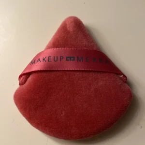 Rosa puder puff från Makeup Mekka - En mjuk och fluffig puder puff i rosa sammet från Makeup Mekka. Puffen har en praktisk rem för grepp och är formad med en spetsig topp för precision vid applicering av puder eller foundation.