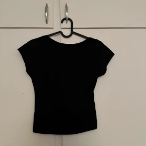 Svart topp från Bik Bok - Säljer en svart topp från Bik Bok med öppen rygg och korta ärmar. Enkel och stilren design som passar perfekt till många olika outfits.