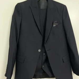 Svart kostym från Esseal med väst - Säljer en svart kostym från Esseal i slim fit med matchande väst. Kostymen är tillverkad i en ullmix och har klassisk kavaj med två knappar, fickor och bröstnäsduk. Perfekt för bal eller fest.