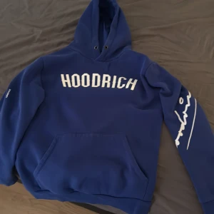Blå hoodie från Hoodrich - Säljer en blå hoodie från Hoodrich med vit text på bröstet och ärmen. På ryggen står det 'FROM NOTHING TO SOMETHING' i vitt. Hoodien har huva och magficka, perfekt för en avslappnad stil.