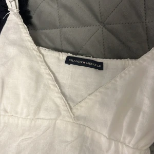 Vit topp med knyt från Brandy Melville - Säljer en vit topp från Brandy Melville med v-ringning och smala axelband. Tröjan har knyt i ryggen och är tillverkad i ett lätt linnematerial, perfekt för varma dagar. Köpt för runt 250kr.