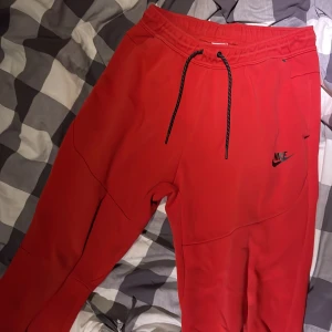 Röda Nike mjukisbyxor med snörning M - Riktigt snygga röda mjukisbyxor från Nike med svart logga på benet. Byxorna har elastisk midja med svart snörning och dragkedjeficka bak. Perfekta för chill eller träning, och materialet känns mjukt och skönt.