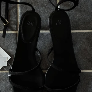 Svarta sandaler med låg klack från H&M - Stilrena svarta sandaler från H&M med tunna remmar och låg klack. Nya och oanvända! De är en aning för små för mig därav jag säljer dem.