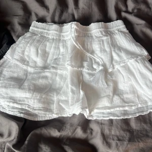 Vita volangshorts med snörning - Superfina vita shorts med volangdetaljer och snörning i midjan med tofsar. Lätta och luftiga i ett tunt bomullstyg, perfekta för varma sommardagar. Elastisk midja för skön passform och flowig känsla.